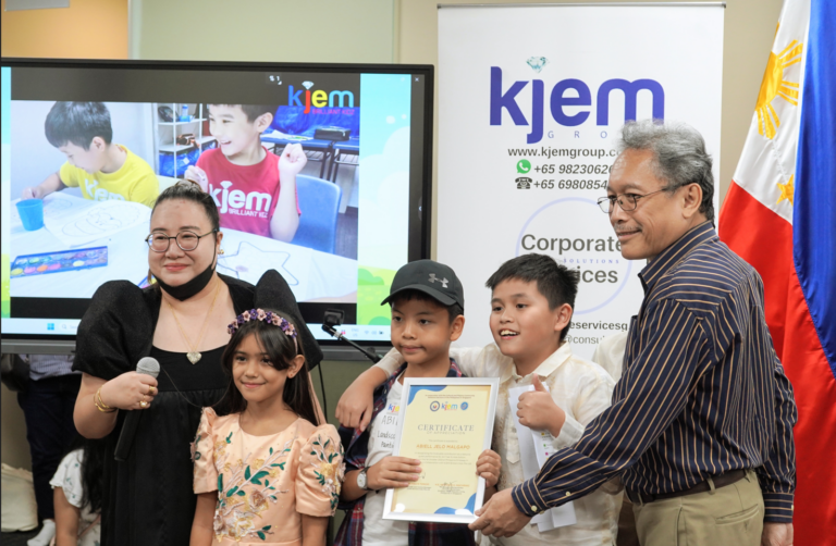 KJEM Founder Meg Nones Tongio, with the afternoon’s emcees Shana and JP, pose with Abiel 
as he receives his Certificate of Participation from Ambassador Macaraig.